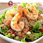 A vibrant Shrimp & Quinoa Salad featuring plump grilled shrimp, mixed greens, red tomatoes, and quinoa, garnished with lemon zest and herbs, presented in a white square bowl with the 'Strange Sculpting' logo at the top left corner.