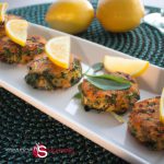 Golden-brown salmon and sweet potato cakes garnished with lemon slices on a white plate, set against a green placemat with whole lemons in the background