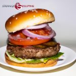 Healthy beef burger with lettuce, tomato, onion, and Greek yogurt sauce on a white plate with Strange Sculpting logo