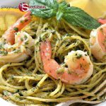 Protein-rich pasta coated with green pesto, topped with succulent grilled shrimp and a garnish of fresh basil, served with a slice of lemon on the side