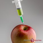 A syringe injecting a green substance into a red apple