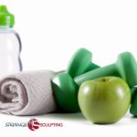 A fitness still life featuring a rolled-up grey towel, a green water bottle, a pair of green dumbbells, and a green apple on a white background with the logo 'STRANGE SCULPTING' at the bottom.